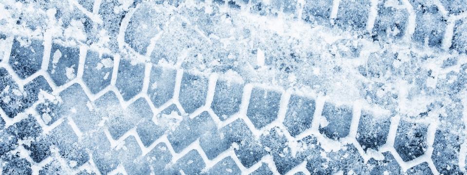 Detailaufnahme von Reifenspuren auf einer eisigen, verschneiten Straße.