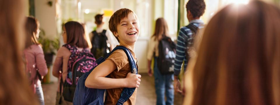 Symbolbild: Mehrere Kinder in einem Schulflur, ein Schüler schaut lächelnd zurück.