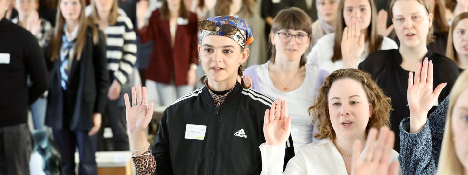 Junge Frauen und Männer stehen in einer Gruppe und haben die Hand zum Eid erhoben.