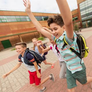 Schülerinnen und Schüler laufen fröhlich über einen Schulhof.