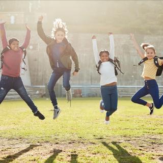 Eine Gruppe Kinder springt auf einer Wiese in die Luft.