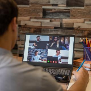 Junge sitzt vor einem Laptop auf dem eine Videokonferenz läuft.