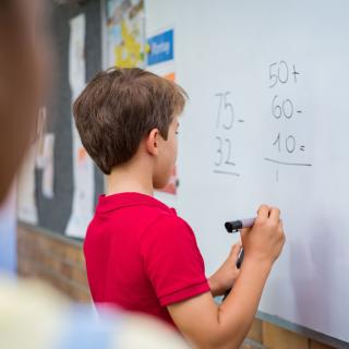Grundschüler löst eine Mathematikaufgabe an der Tafel.
