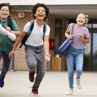 Schüler laufen lachend aus Schulgebäude.