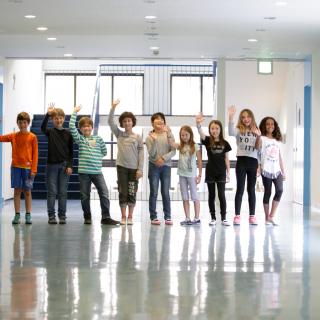 Schülerinnen und Schüler der Deutschen Schule Tokyo Yokohama stehen im Schulflur und winken