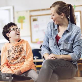 Lehrerin und Förderschulkind lächeln sich an.