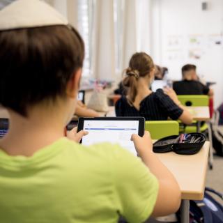 Eine Junge mit Kippa schaut im Unterricht auf sein iPad