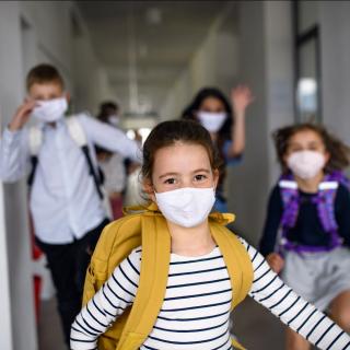 Eine Gruppe Schülerinnen und Schüler läuft Alltagsmasken tragend einen Schulflur entlang.