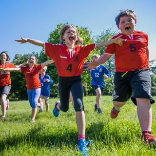 Kinder und Jugendliche in Sportkleidung rennen über eine Wiese