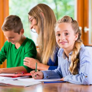 Zwei Kinder arbeiten in einer Lerngruppe zusammen mit einer Lehrerin.