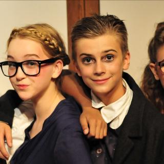 Drei Kinder posieren für eine Theateraufführung, sie sind für ihre Rollen kostümiert und mit Theaterschminke geschminkt.