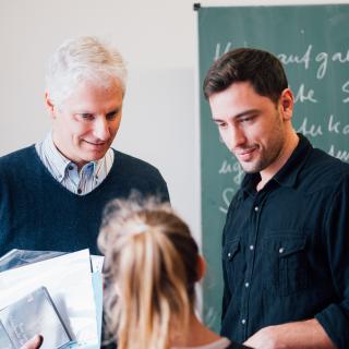 Ein älterer und ein jüngerer Lehrer unterhalten sich mit einer Schülerin.