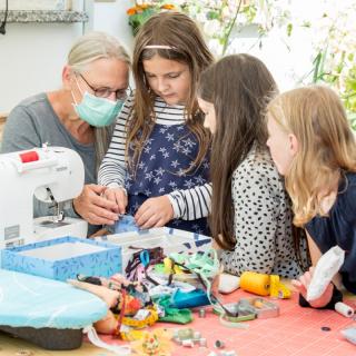 Drei Kinder und eine Frau sitzen gemeinsam an einer Nähmaschine.