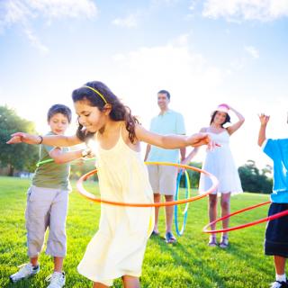 Eine Familie spielt auf der Wiese mit Hula Hoop-Reifen