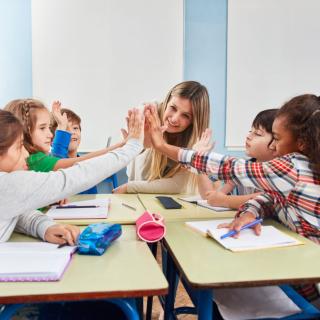 Eine Lerngruppe sitzt mit ihrer Lehrerin am Tisch.