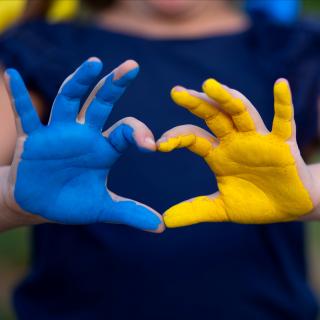 Blau und gelb bemalte Hände formen ein Herz