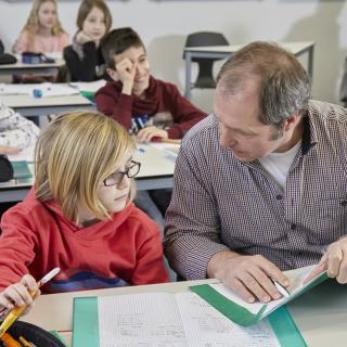 Unterrichtssituation: Ein Lehrer sitzt neben einem Schüler und erklärt ihm etwas. 
