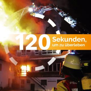 Ein Feuerwehrmann steht vor einem brennenden Haus.