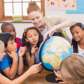 Eine Schülergruppe betrachtet zusammen mit einer Lehrerin einen Globus.