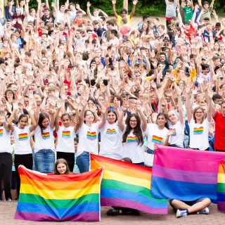 Die ganze Schulgemeinde des GKGE Troisdorf steht mit Regenbogenflaggen auf dem Schulhof.