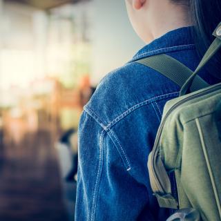 Rückansicht eines Mädchens mit Rucksack vor einem Klassenraum.