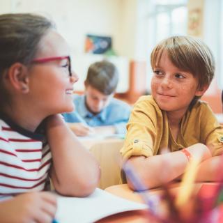 Grundschülerinnen und Grundschüler sitzen an einem Tisch im Unterricht und bearbeiten gemeinsam eine Aufgabe.