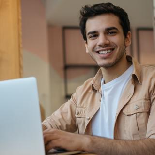 Ein Mann sitzt vor einem geöffneten Laptop und schreibt etwas.