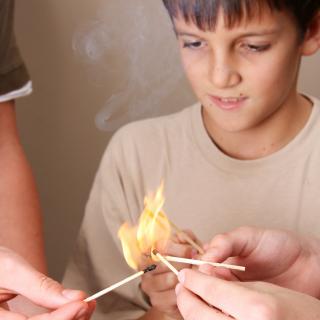 Mehrere Hände halten brennende Streichhölzer zusammen, zu erkennen ist in der Mitte nur ein Kind, das ebenfalls ein Streichholz in die große Flamme streckt. 