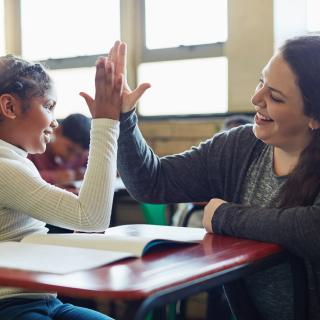 Schülerin und Lehrerin berühren ihre Hände in einer "High Five"-Geste. Beide lächeln dabei.