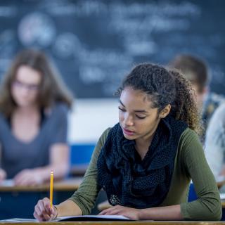 Jugendliche sitzen in einem Klassenraum an Tischen und schreiben.