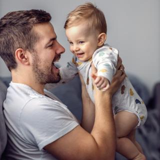 Ein Vater hebt seinen Säugling lächelnd hoch.