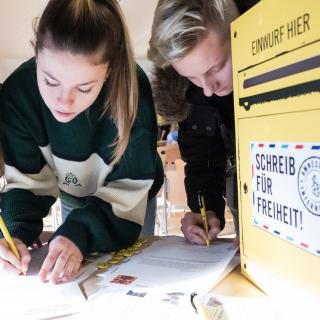 Drei Schülerinnen und Schüler schreiben im Rahmen des Amnesty International-Briefmarathons einen Brief.