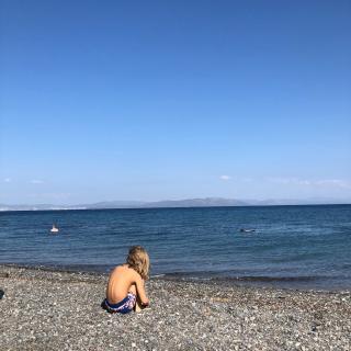 Ein Junge sitzt am Strand und schaut aufs Wasser.