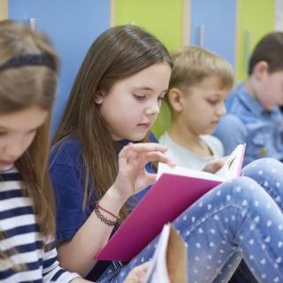 Grundschulkinder, die auf dem Boden sitzen und in Büchern lesen.