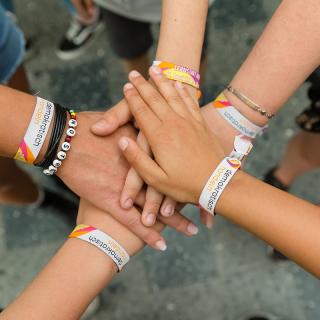 Die Hände von Jugendlichen mit "Demokratisch Handeln"-Armbändchen treffen sich.