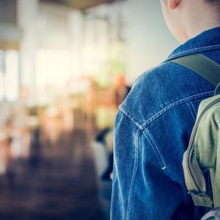 Schülerin mit Rucksack schaut auf einen leeren Schulflur