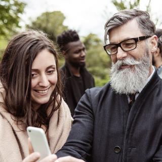 Ein älterer Mann schaut mit mehreren jungen Frauen aufs Smartphone.