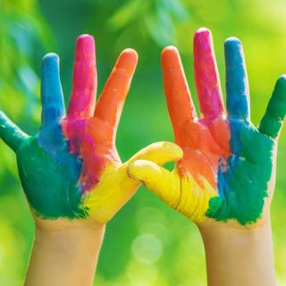 Zwei in Regenbogenfarben bemalte Kinderhände werden hochgehalten.
