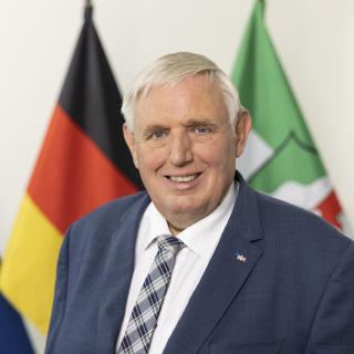 Minister Karl Josef-Laumann steht vor den Flaggen von Europa, Deutschland und NRW.