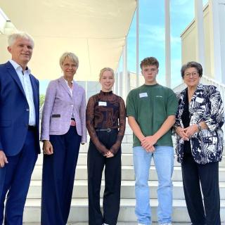 Gruppenbild mit Professor Axel Görlitz, Studiendekan der Mathematisch-Naturwissenschaftlichen Fakultät an der Düsseldorfer Universität, Ministerin, Preisträgerin Hannah Scholten, Preisträger Luis Rosier und Professorin Ingeborg Henzler, Vorstandsmitglied der Dr.-Hans-Riegel-Stiftung, vor einer Treppe zur Dr. Hans Riegel-Fachpreisverleihung 