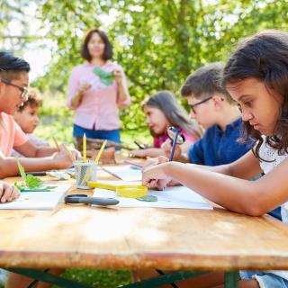 Eine Gruppe von Kindern sitzt draußen an einem Tisch und malt.