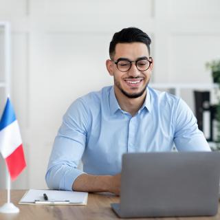 Ein junger Mann sitzt mit einer Frankreich-Flagge neben sich am Schreibtisch.