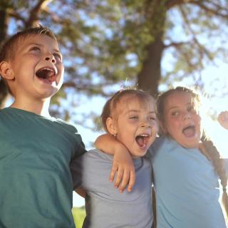 Drei Kinder stehen vor Bäumen und singen laut.