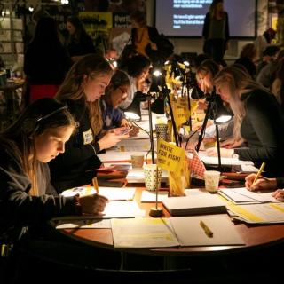 Schülerinnen und Schüler sitzen mit Leselampen an Tischen und schreiben Briefe im Rahmen des Briefmarathons von Amnesty International.