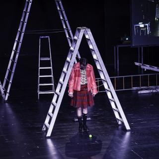 Eine Jugendliche auf der Theaterbühne unter einer Leiter.
