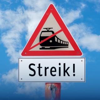 Straßenschild vor blauem Himmel mit der grafischen Darstellung eines durchgestrichenen Zuges. Darunter steht auf einem Schild "Streik!".