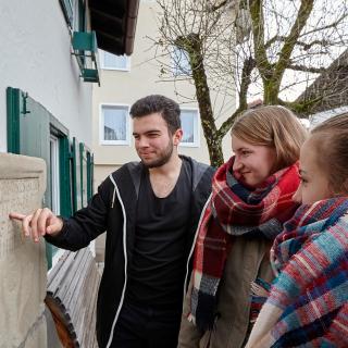 Drei  Jugendliche entziffern die Inschrift auf einem Epitaph.