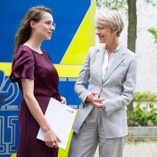 Ministerin Dorothee Feller im Gespräch mit einer Absolventin der FOS-Polizei, die ihr Abschlusszeugnis in der Hand hält.