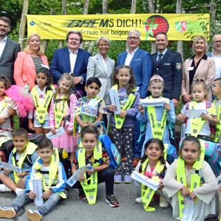 Gruppenbild von Ministerin Dorothee Feller mit Vertreterinnen und Vertretern der Landesverkehrswacht und Schülerinnen und Schülern, im Hintergrund ein Banner mit der Aufschrift "Brems Dich! Schule hat begonnen!"