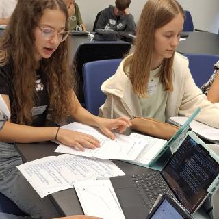 Schülerinnen und Schüler sitzen an einem Tisch mit Laptops und Unterlagen und testen das Lernen mit KI-Unterstützung.